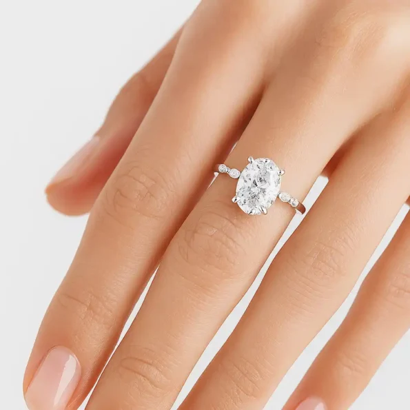 Elegant oval lab-grown diamond engagement ring with marquise side stones in white gold worn on finger