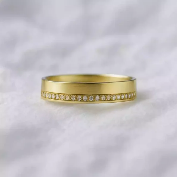 Matte finish yellow gold lab-grown diamond wedding band with flush pave setting on white fabric background