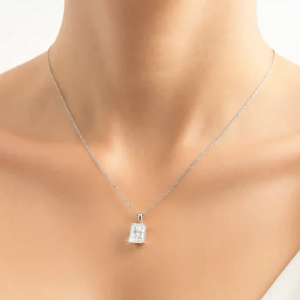 Radiant cut diamond solitaire necklace on model in white outfit for elegant look.